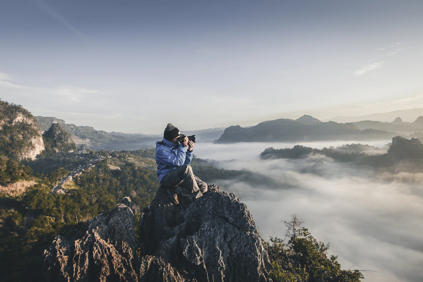 A photographer with a camera standing on a rocky ridge above a sea of clouds