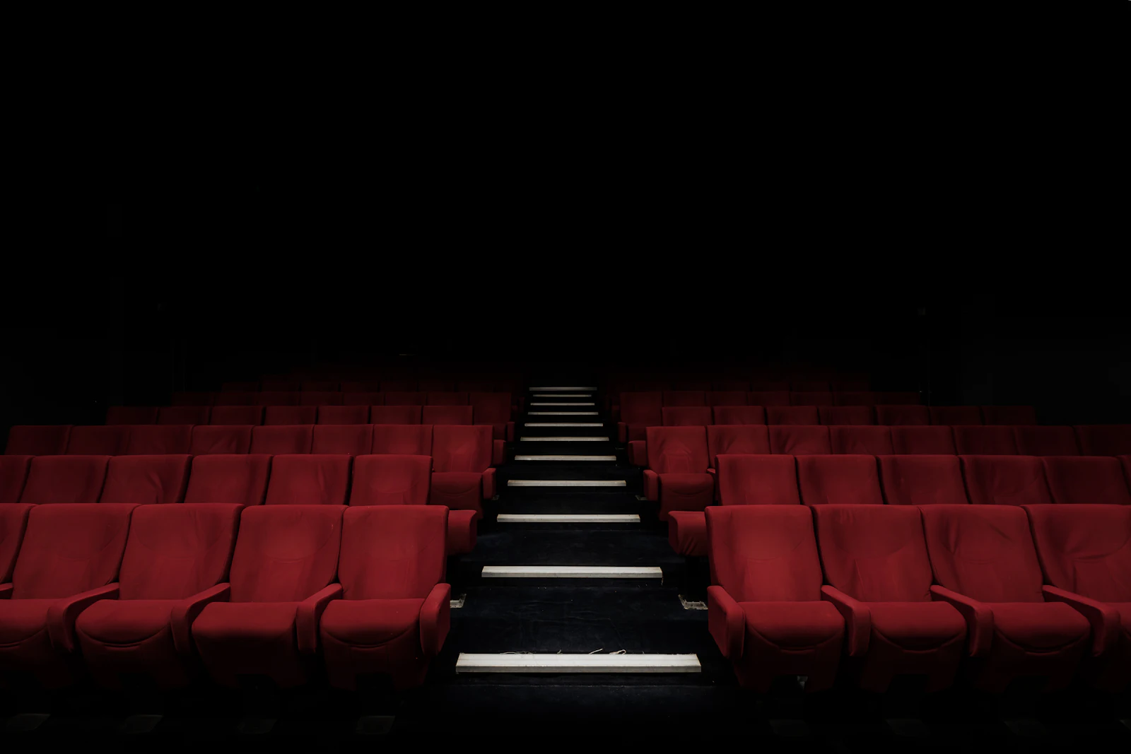 Rows of empty red velvet cinema seats divided by a softly lit aisle