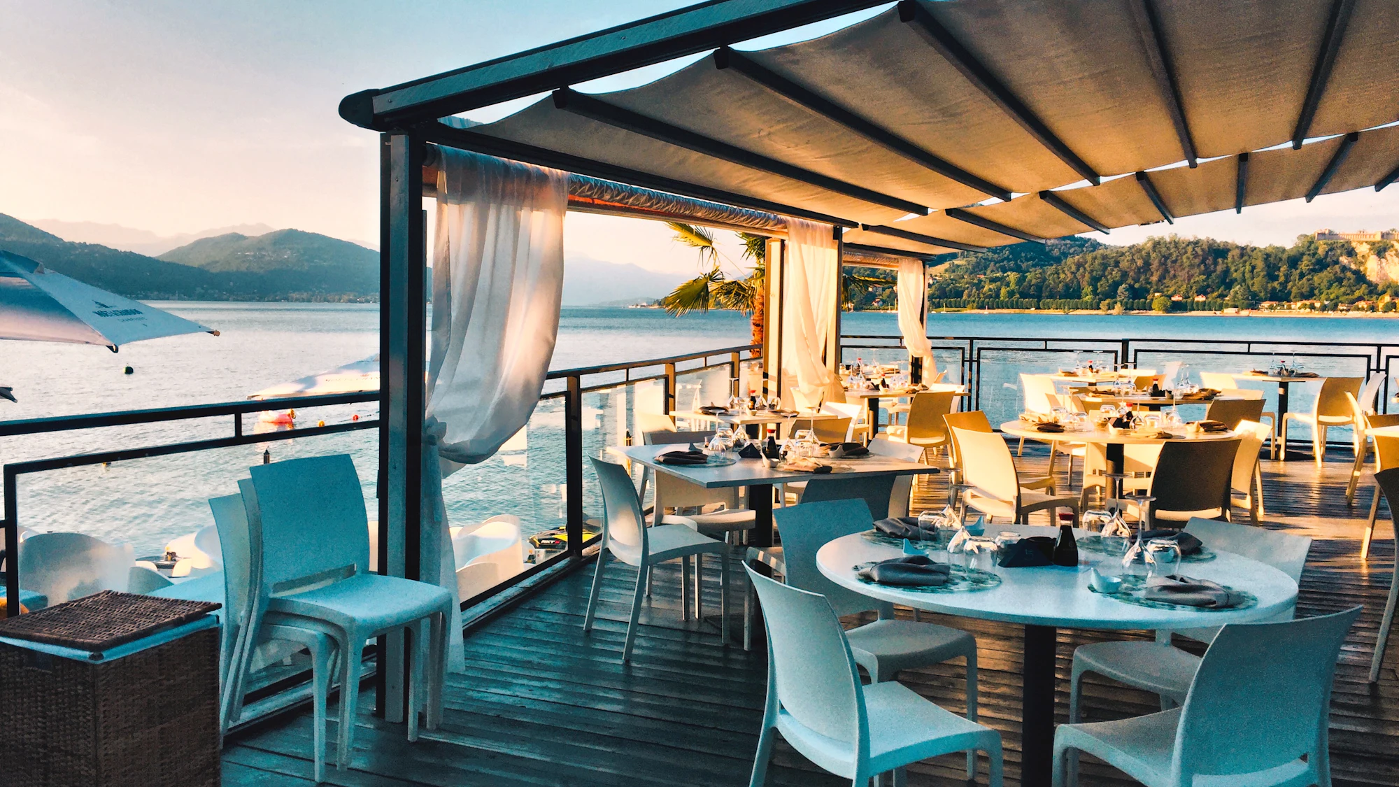 A waterside restaurant terrace set for dinner overlooking a lake and mountains