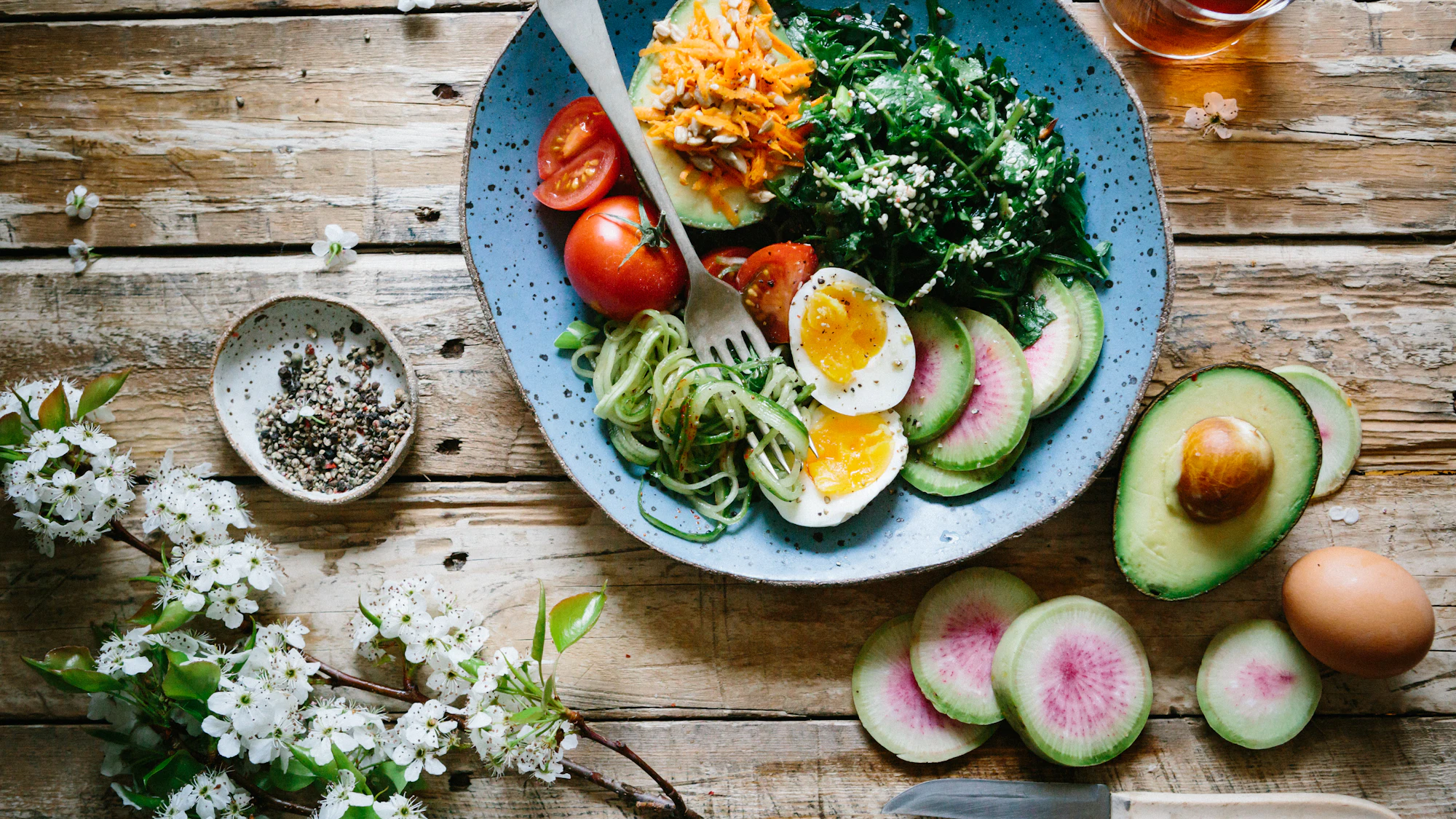 A colourful healthy breakfast bowl with eggs, greens and avocado on a rustic table