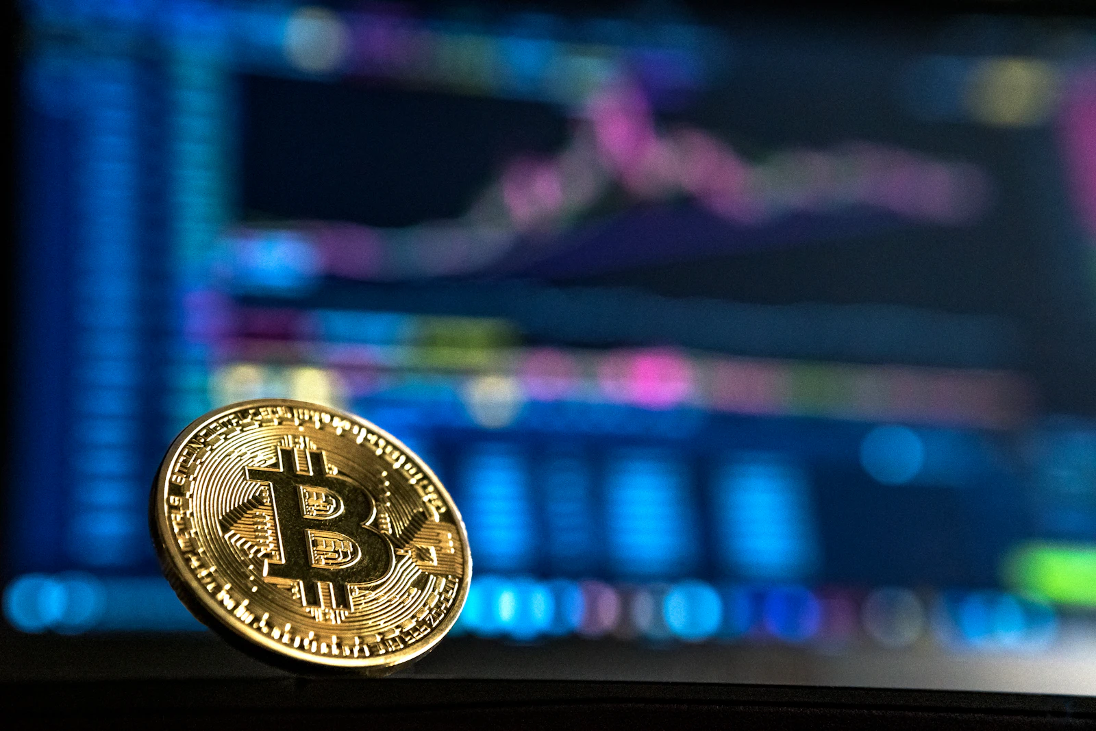 A gold Bitcoin coin standing in front of a glowing trading chart